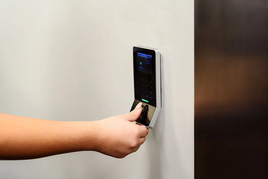 A hand on the fingerprint reader mounted beside the wooden vault door frame